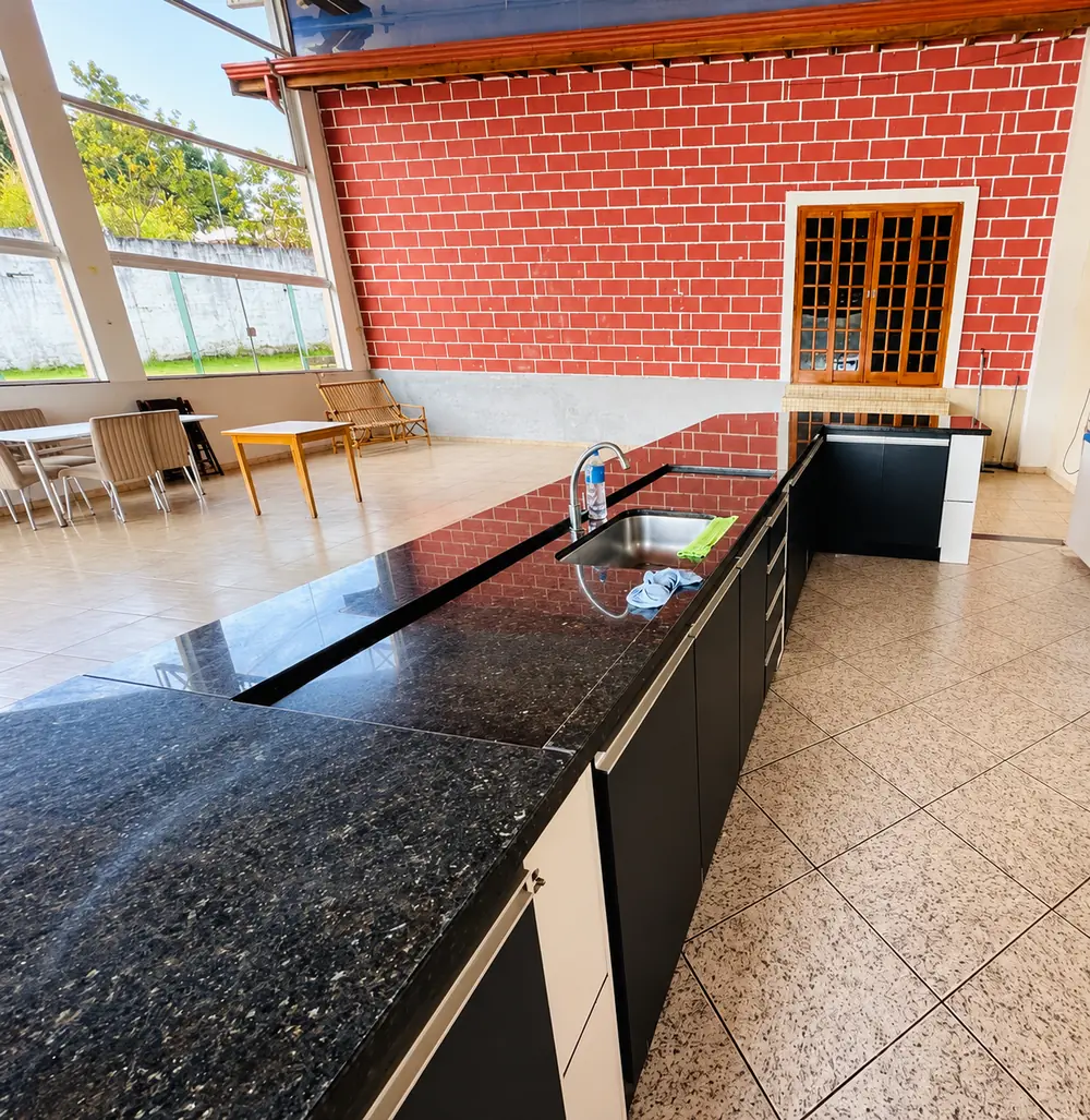 Bancada de granito preto com pia, armários e o salão ao fundo