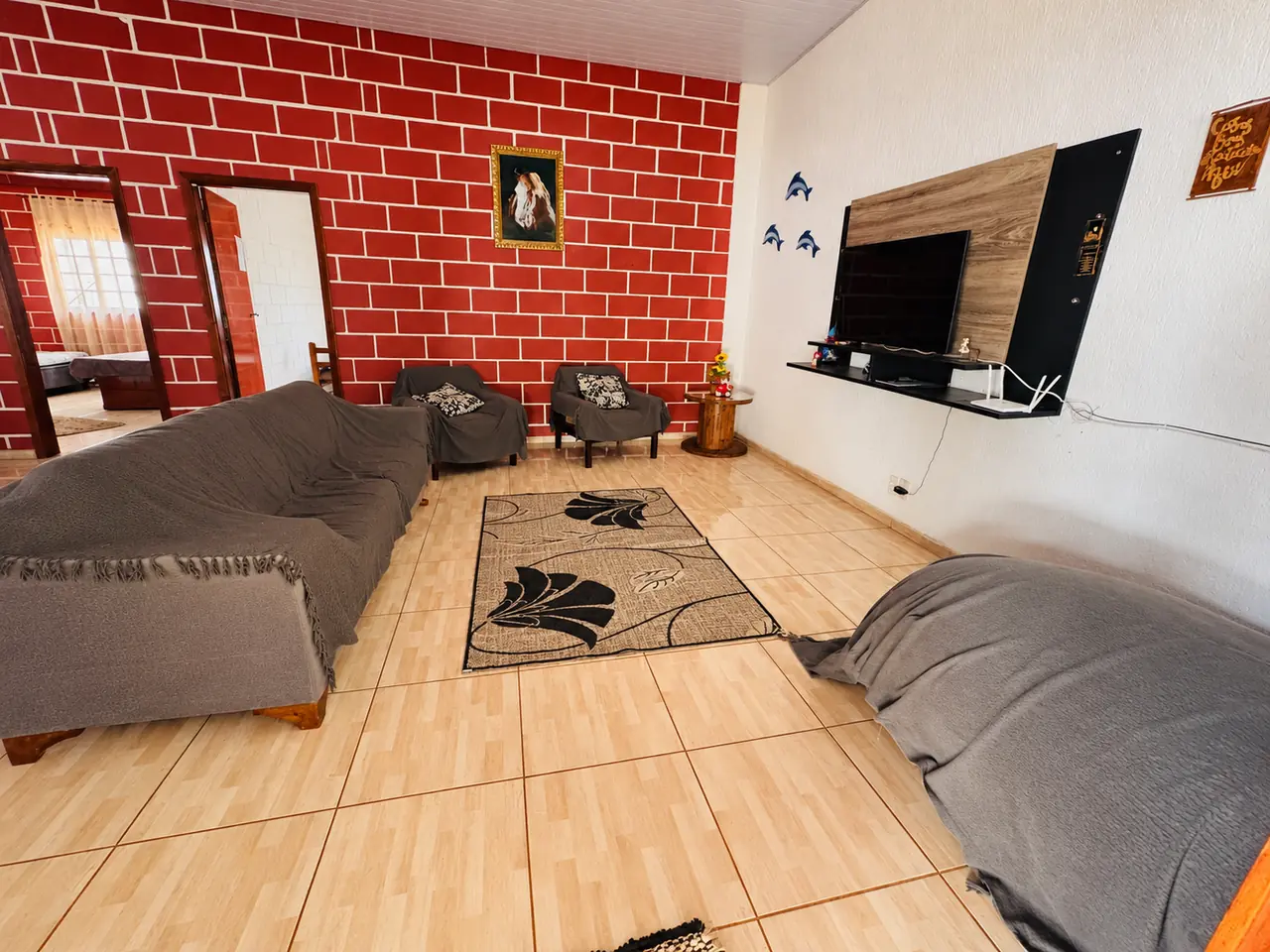 Sala de estar com sofá, poltronas, tapete e TV em painel na parede