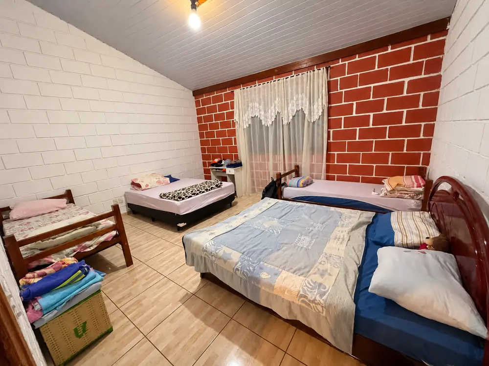 Quarto com cama de casal, camas de solteiro e parede de tijolinho