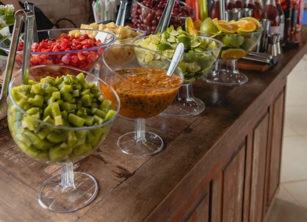 Taças com kiwi, morango, maracujá, limão e laranja e garrafas no balcão de madeira
